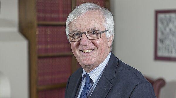 Lord John Shipley, a white-haired man with glasses wearing a dark suit